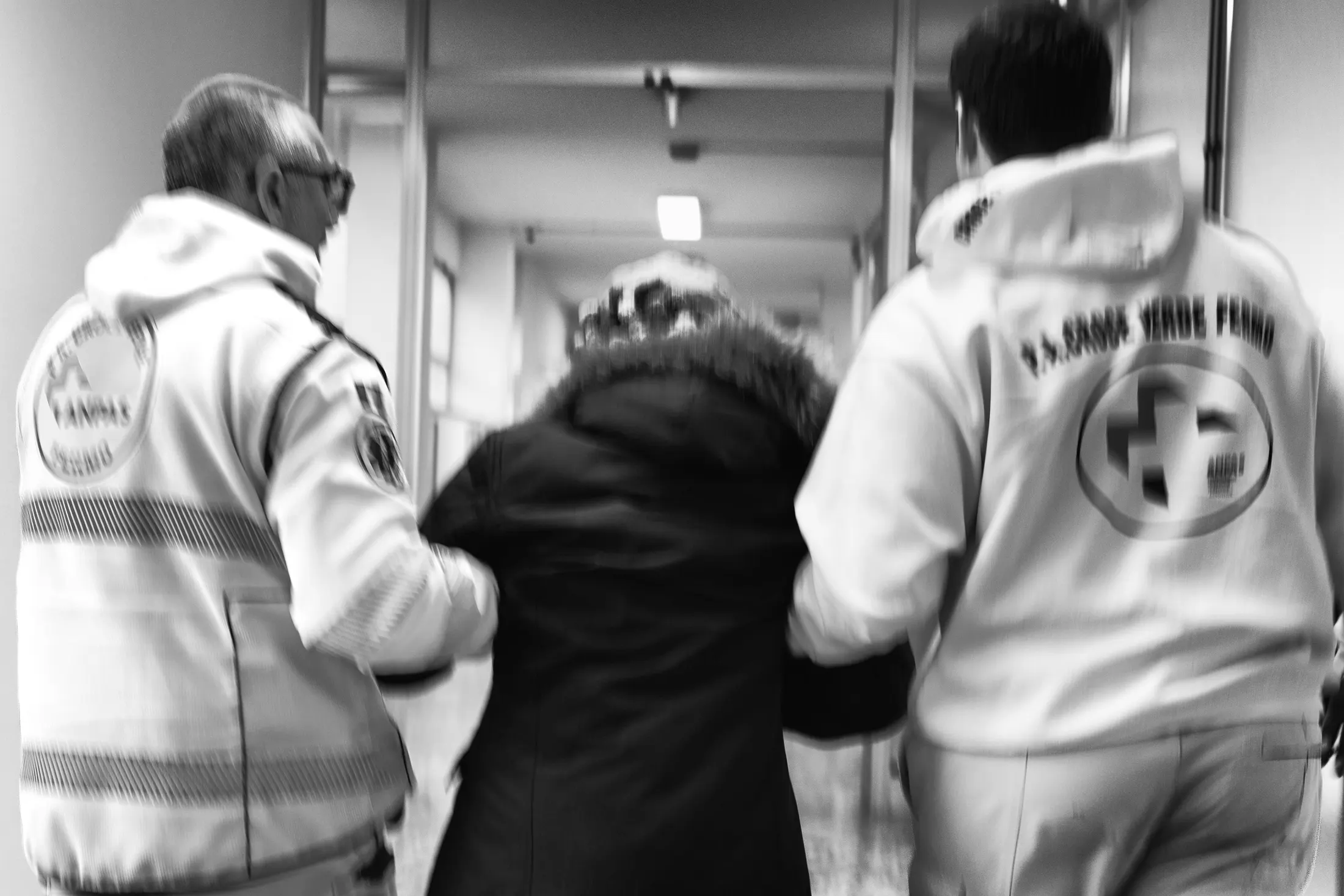 Two volunteers walking a person along a hospital corridor