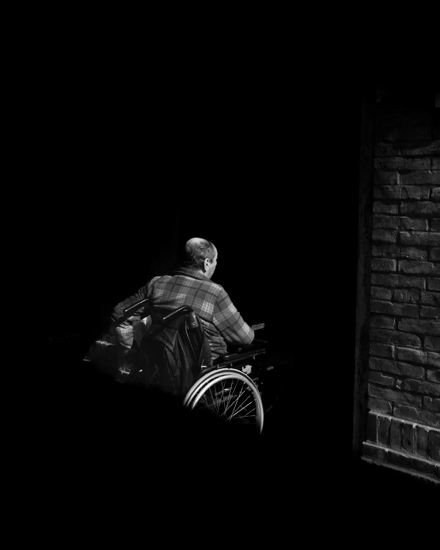 Person in a wheelchair accompanied in the dark, a single light on the subject