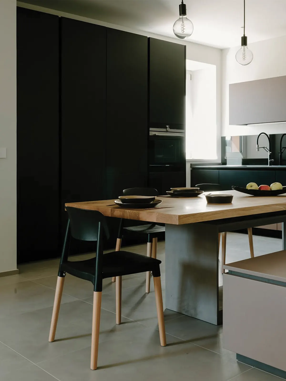 Cucina con isola in legno e sedute nere, lampade a sospensione