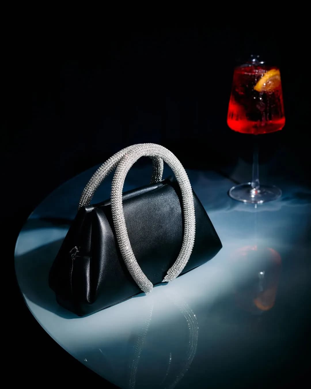 Black bag with a crystal handle beside a glass, night still life