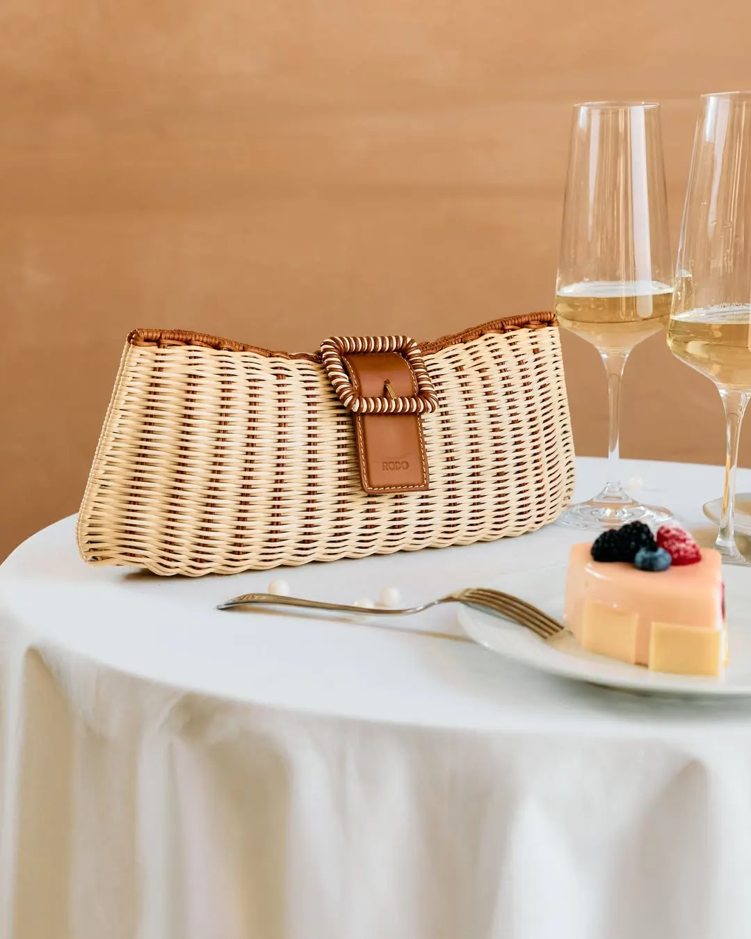 Wicker clutch on a laid table, sparkling wine glasses and dessert