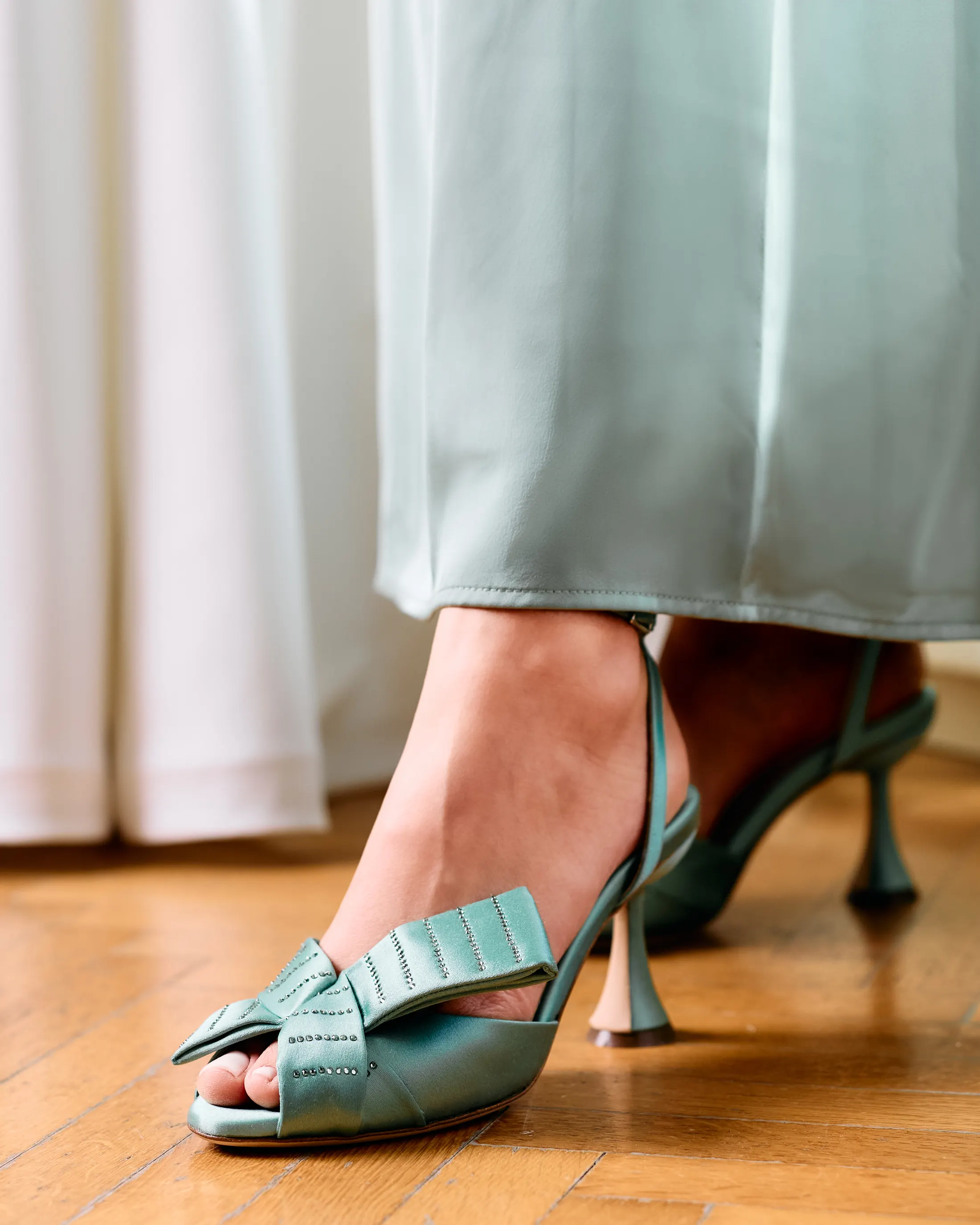 Sage green bow slingbacks on a wooden floor, long satin dress