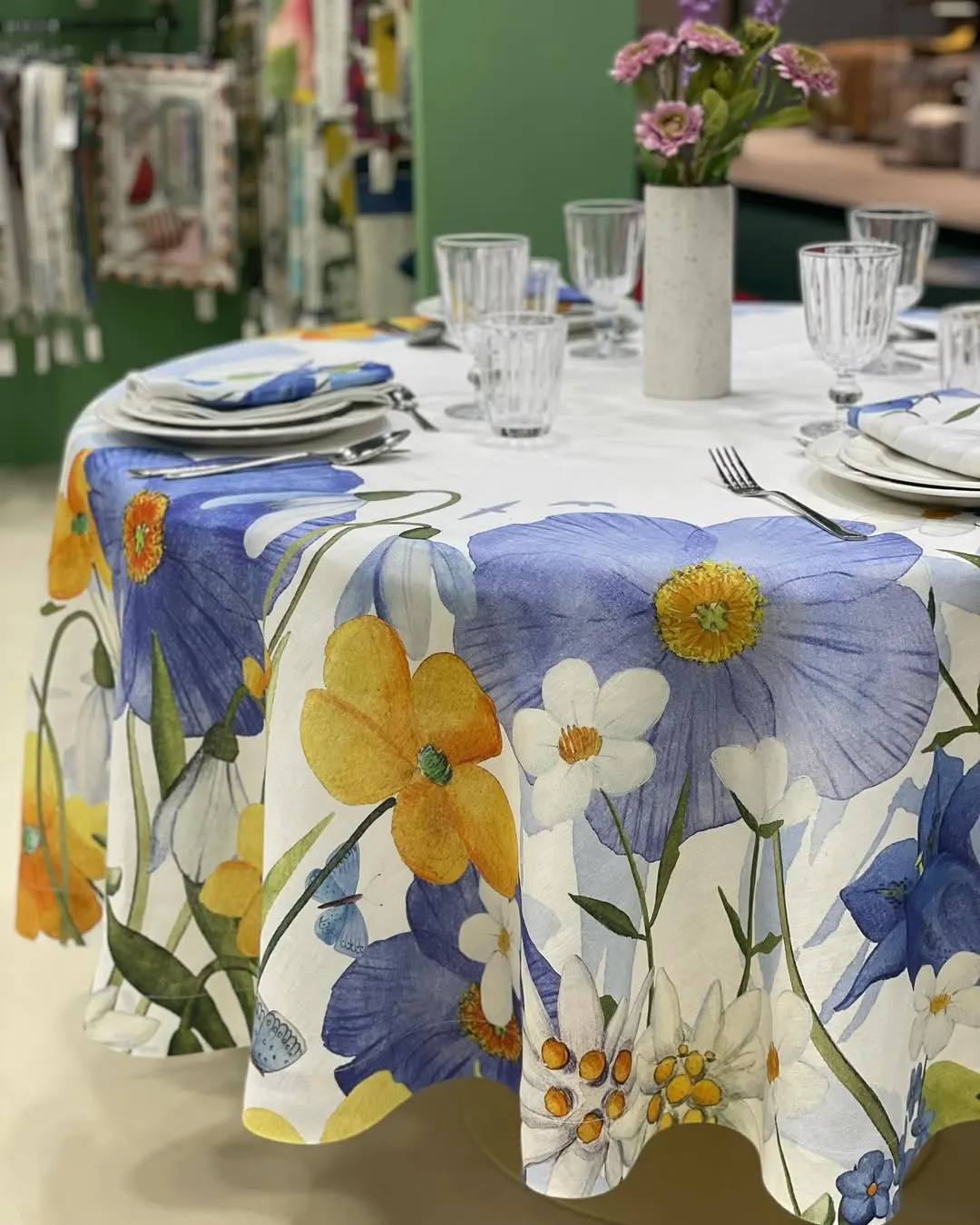 Tavolo rotondo dello stand con tovaglia a fiori blu e gialli, bicchieri e piatti