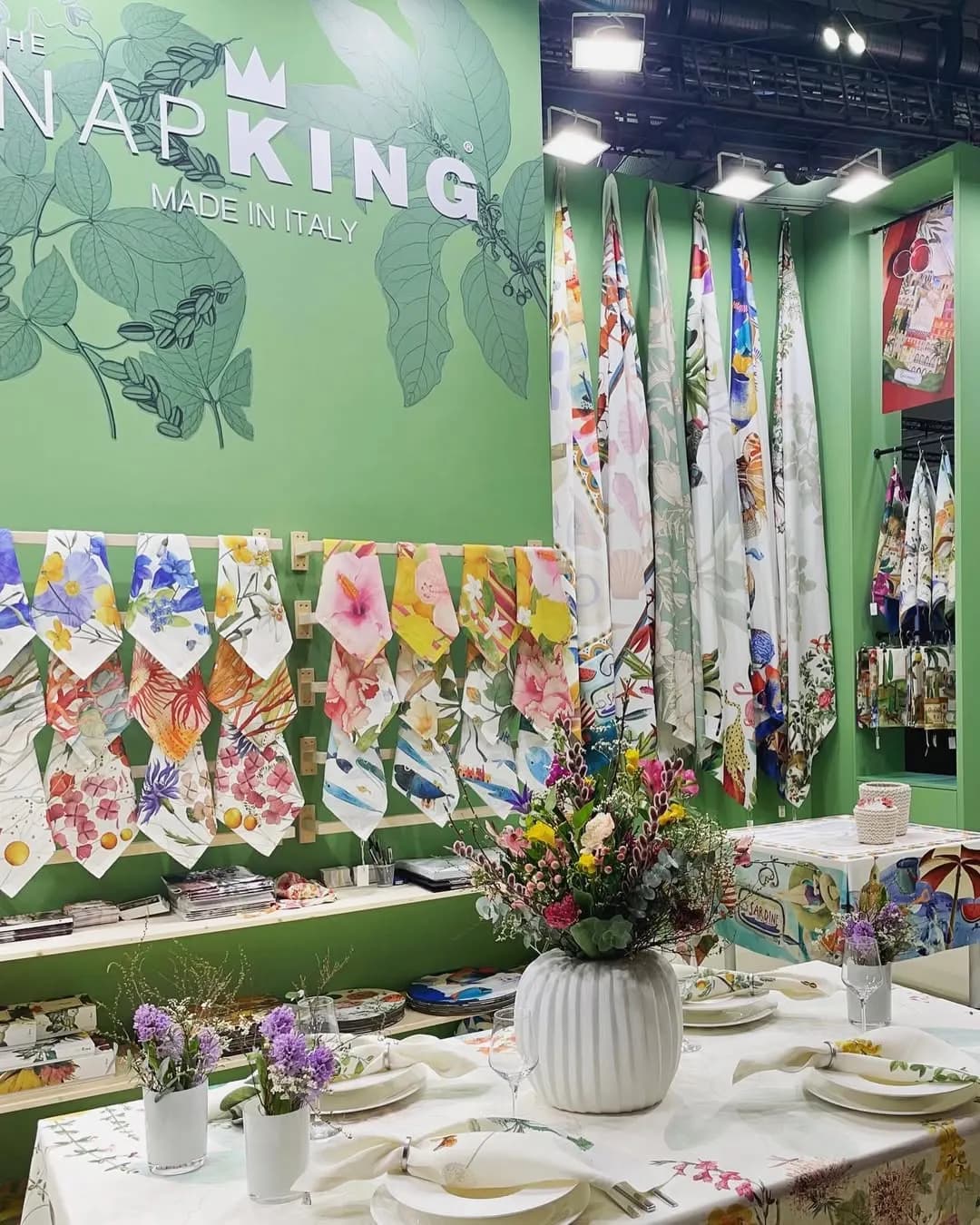 Angolo dello stand con tavola apparecchiata e fiori sotto l’insegna Napking