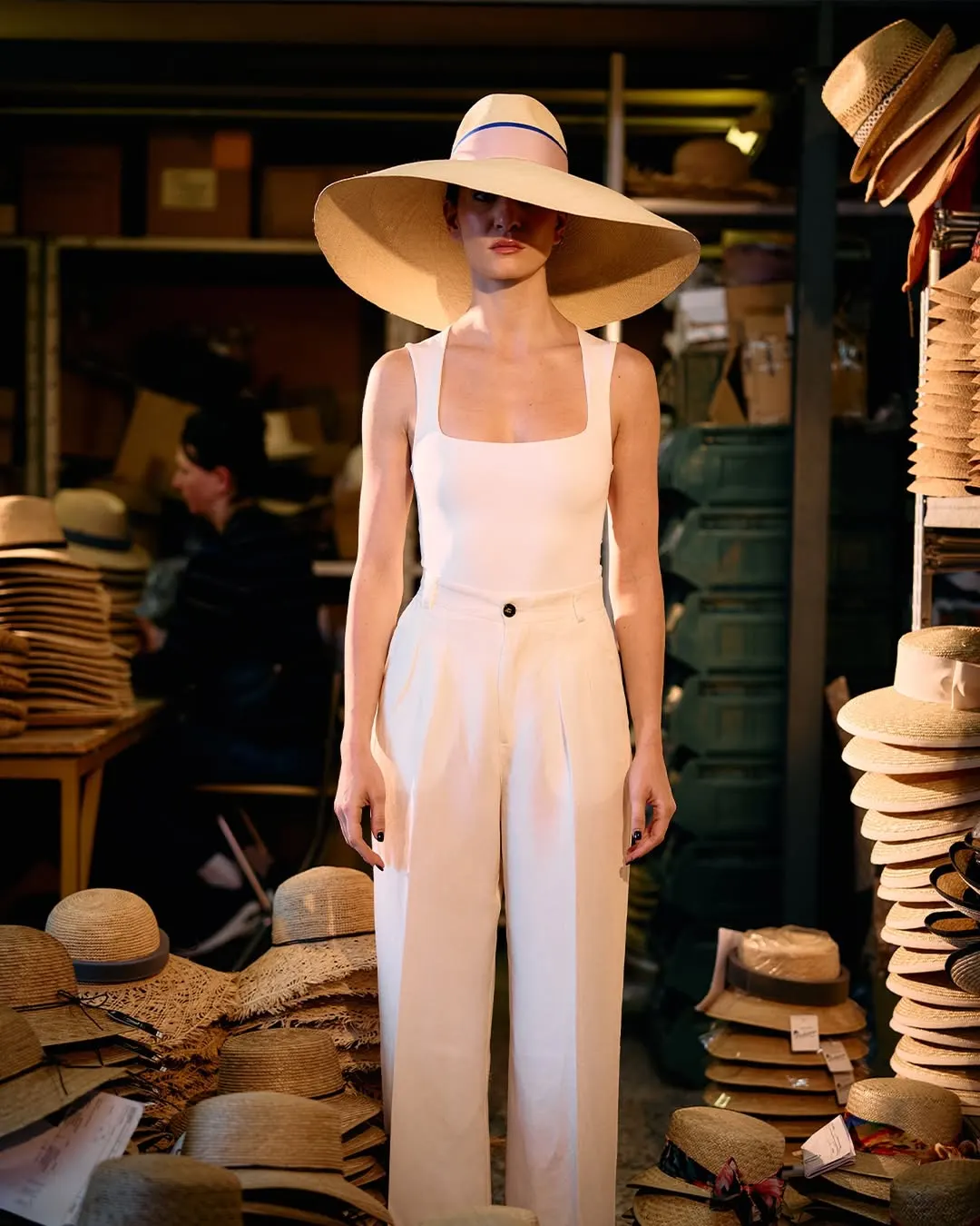 Immagine generata: figura in tuta chiara e cappello di paglia dentro il magazzino delle forme