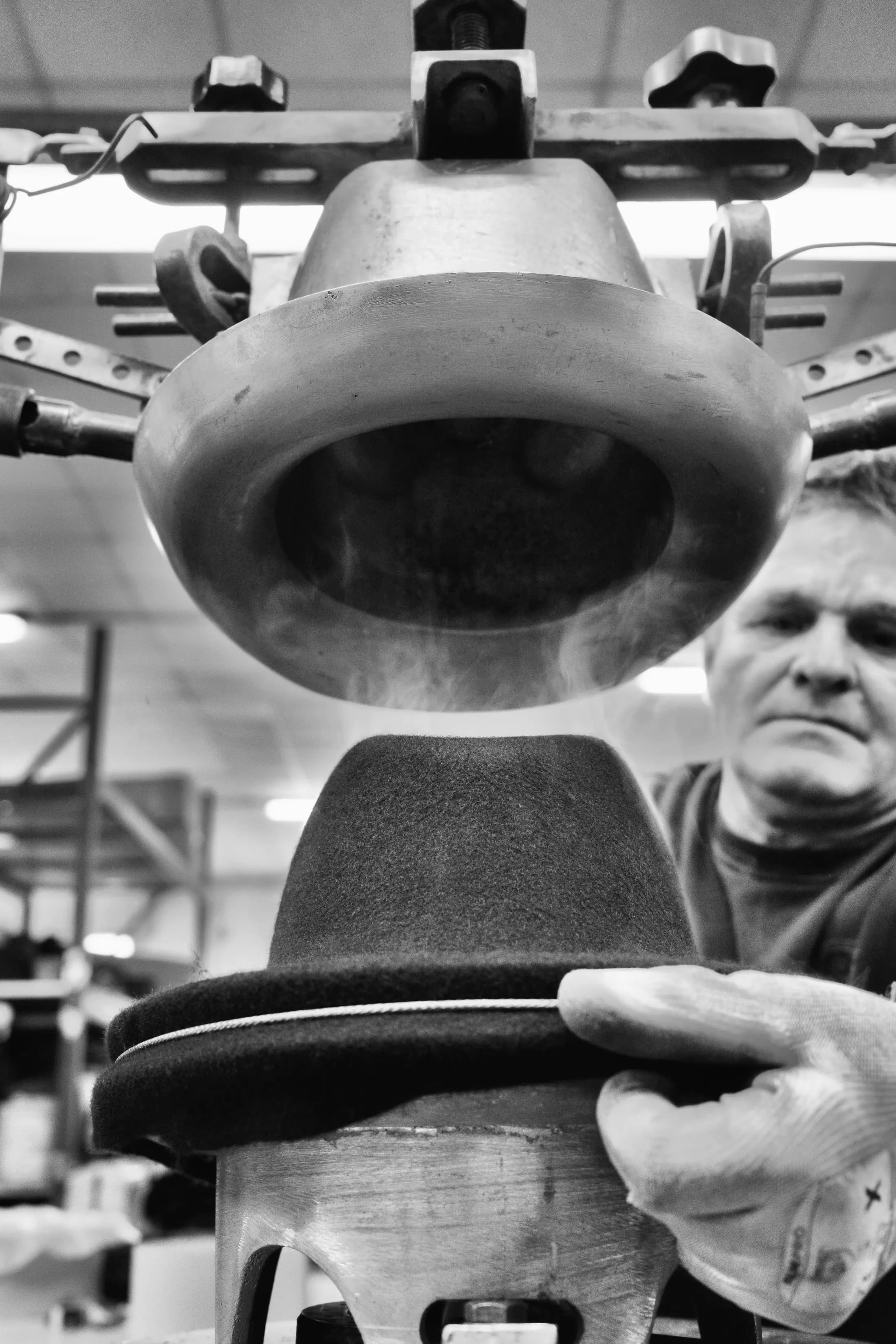 Black hat pressed onto a block, the worker’s hands on the machine