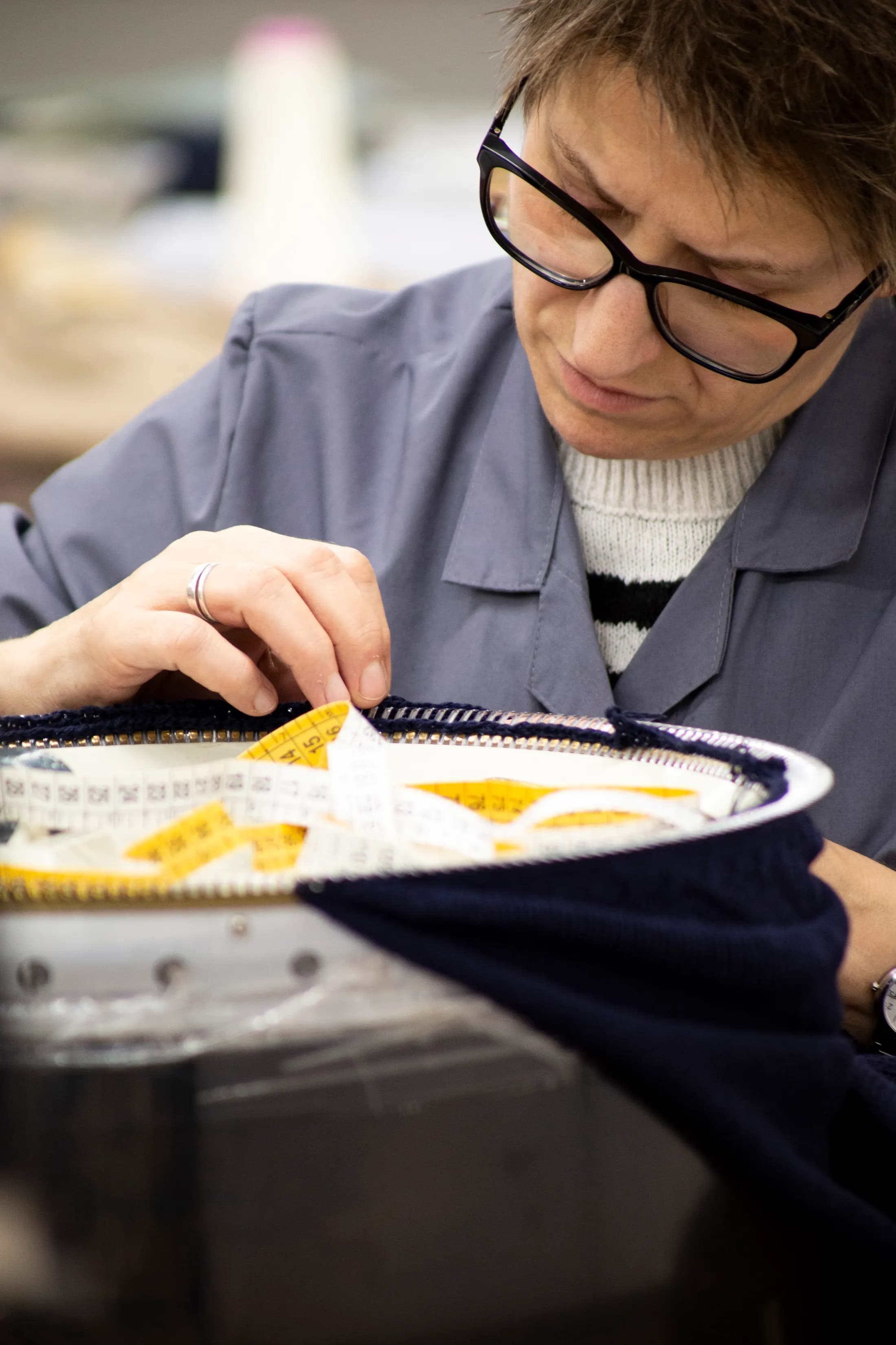 Worker hand-finishing a blue knitted garment with yellow inserts