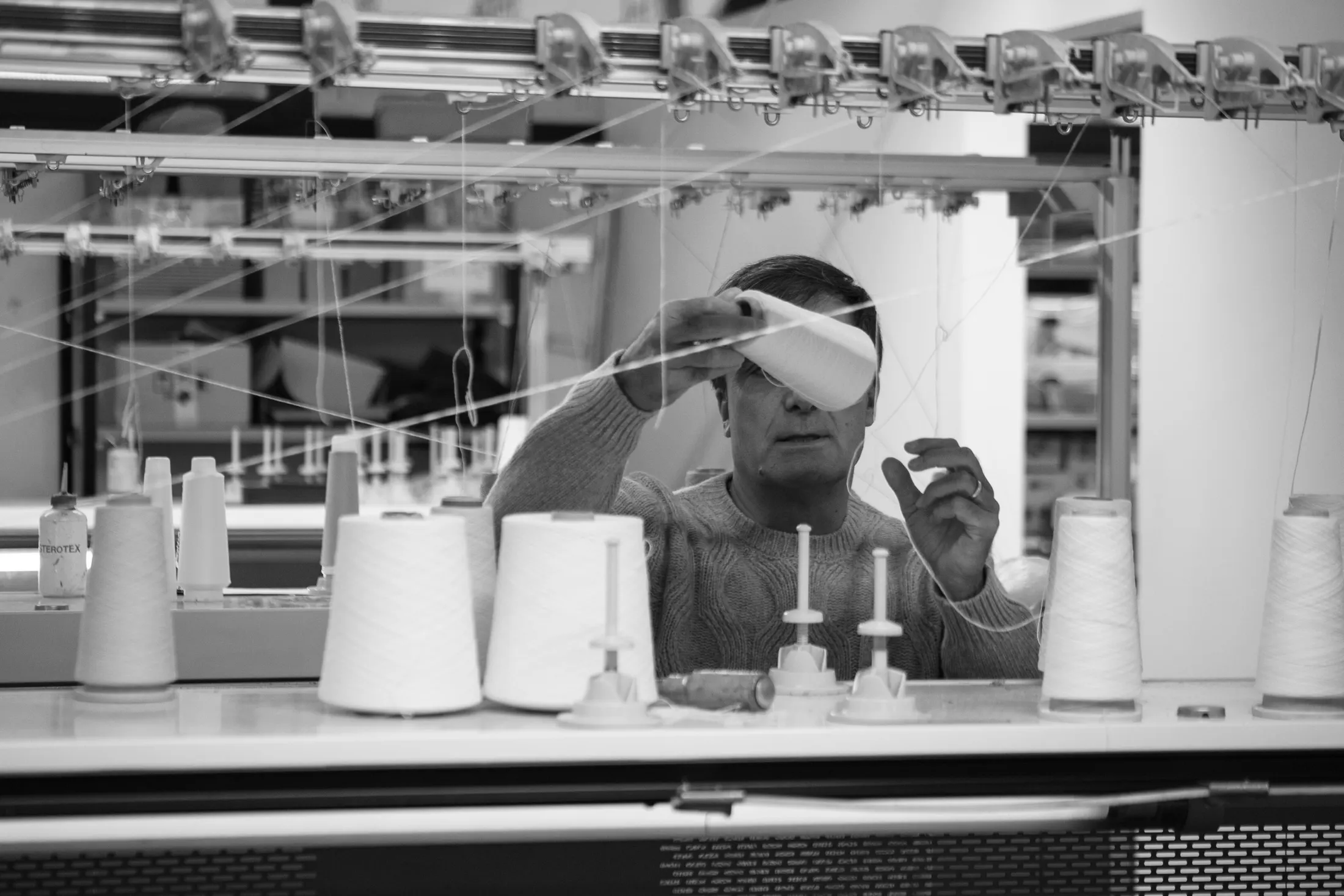 Technician at the circular knitting machine among yarn cones, black and white