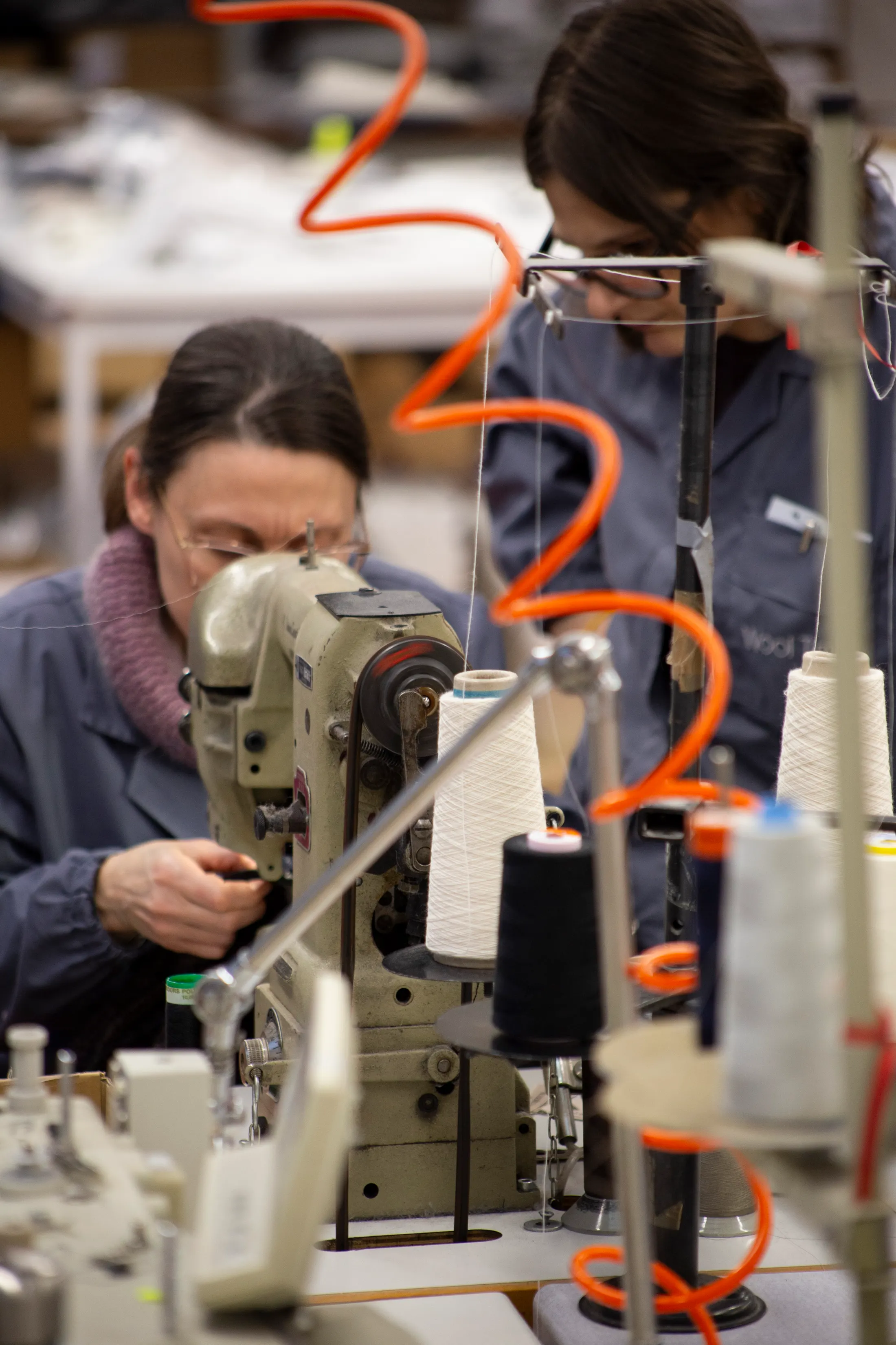 Worker at a sewing machine with orange thread, a second worker behind