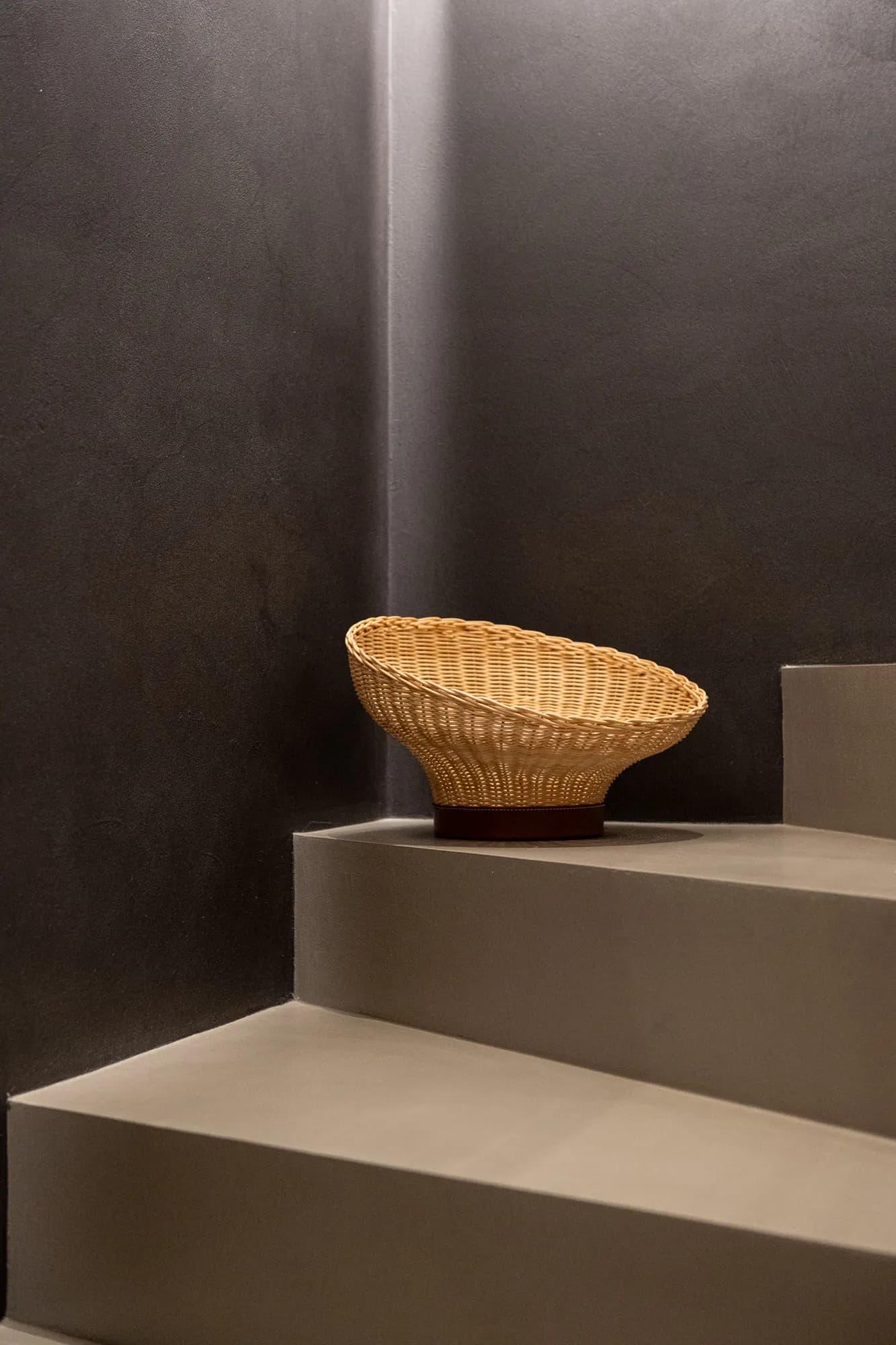 Woven wicker basket on a concrete staircase against a dark brown wall