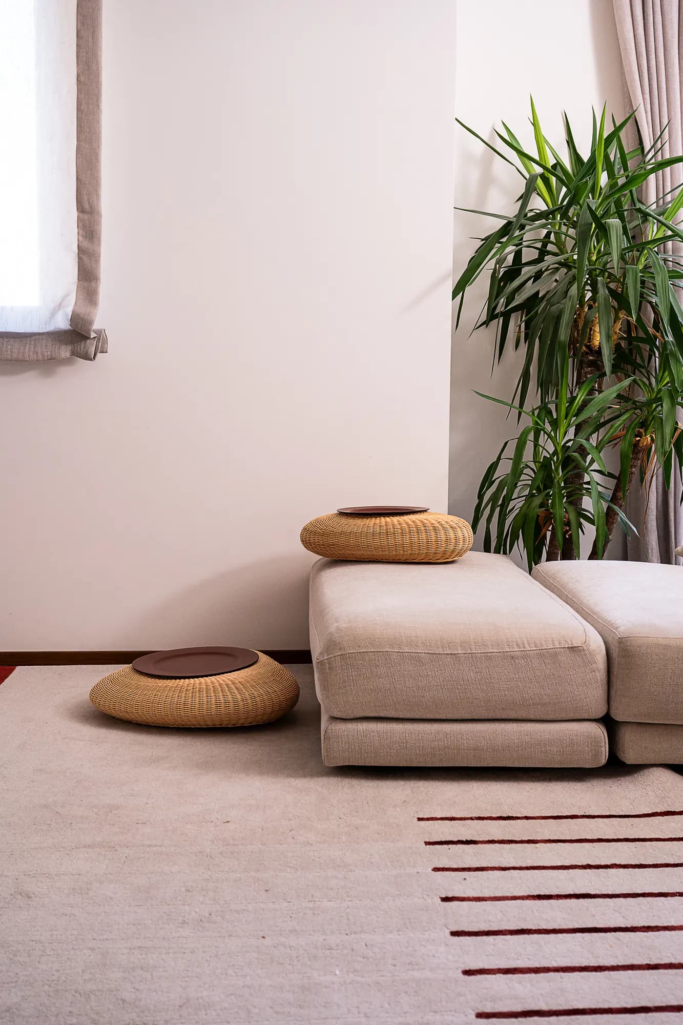Pouf e cuscini intrecciati in una stanza minimale con pianta e tappeto a righe