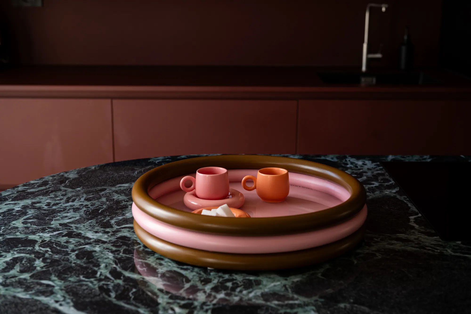 Pink and brass tray on dark green marble in a burgundy kitchen