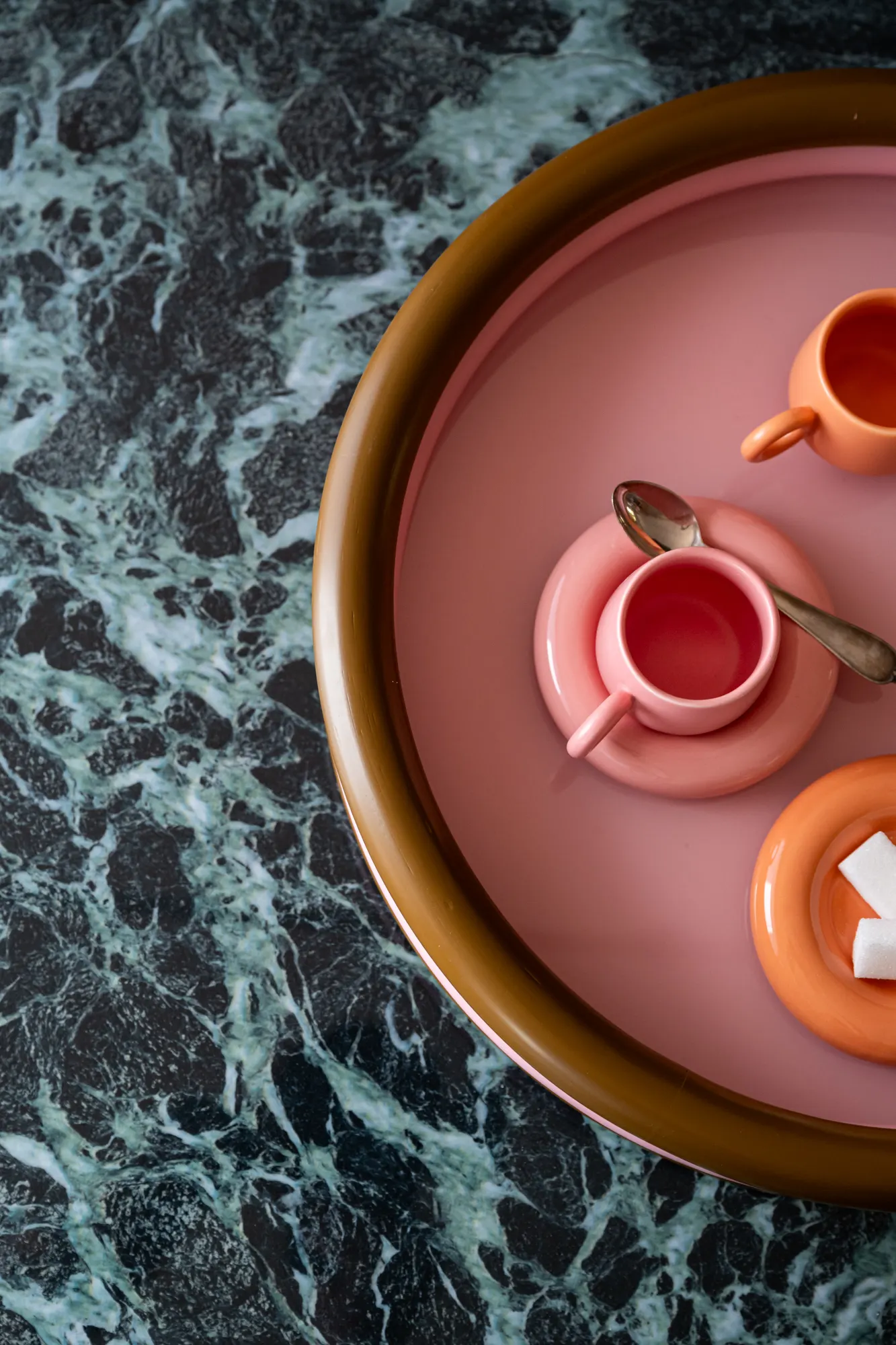 Pink tray with cups seen from above, on veined green marble