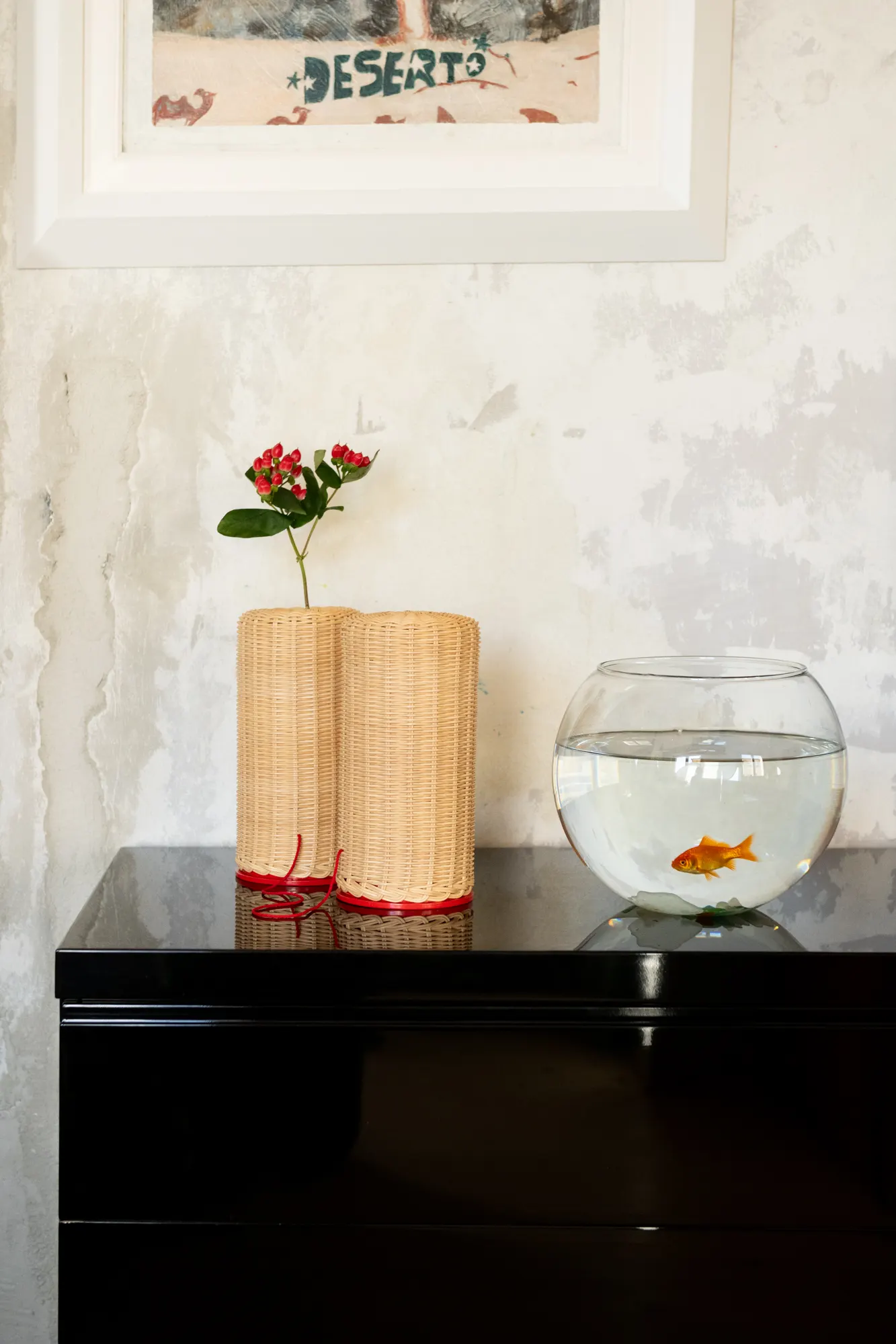 Two rattan lamps and a goldfish bowl on a glossy black sideboard