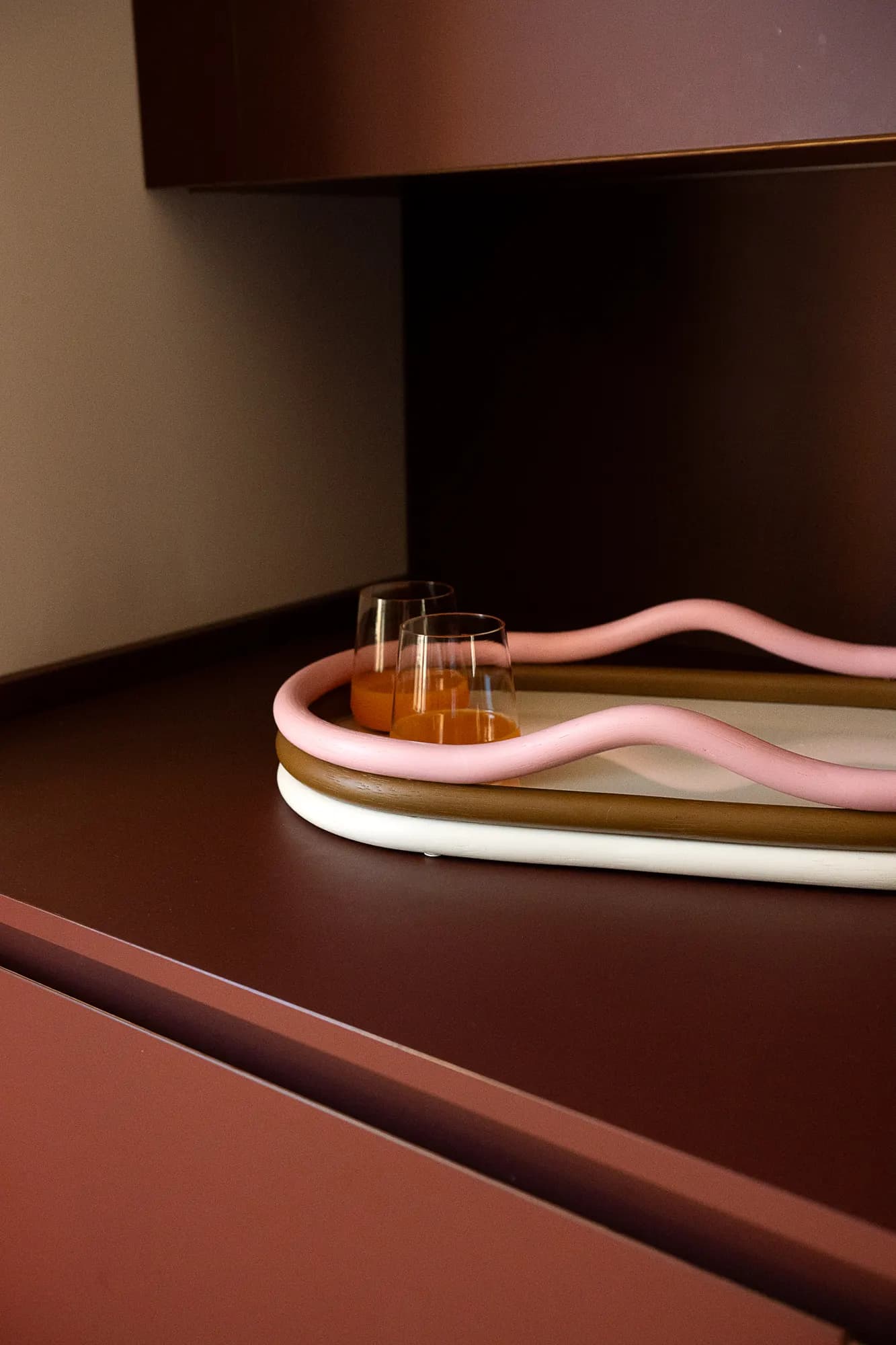 Curved pink tray with glasses on a burgundy surface