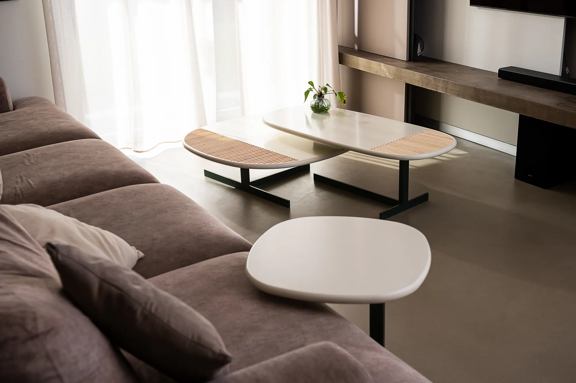 Living room with grey sofa and low tables, light through white curtains