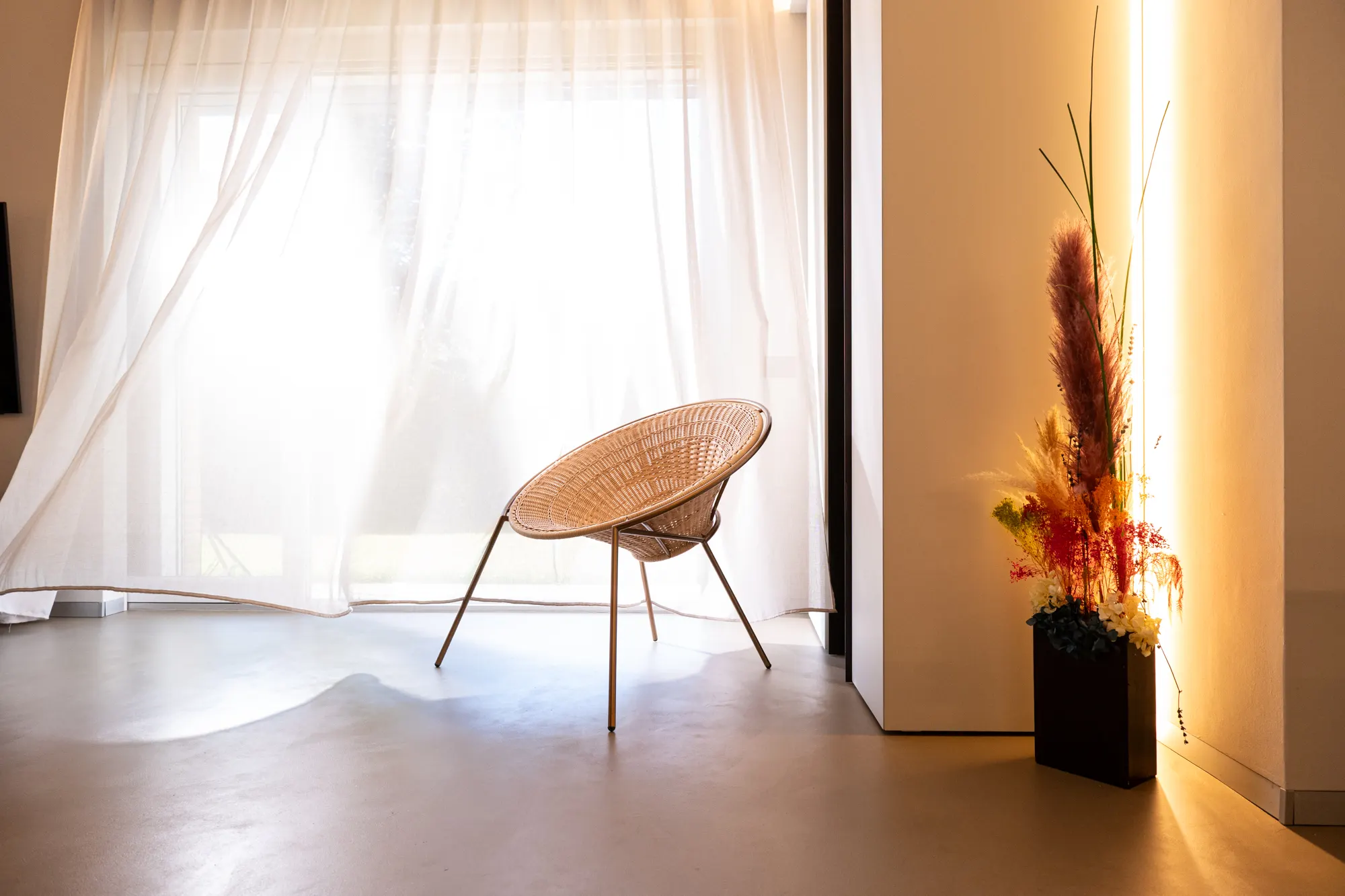 Small woven armchair in front of a curtain, with dried flowers in a black vase
