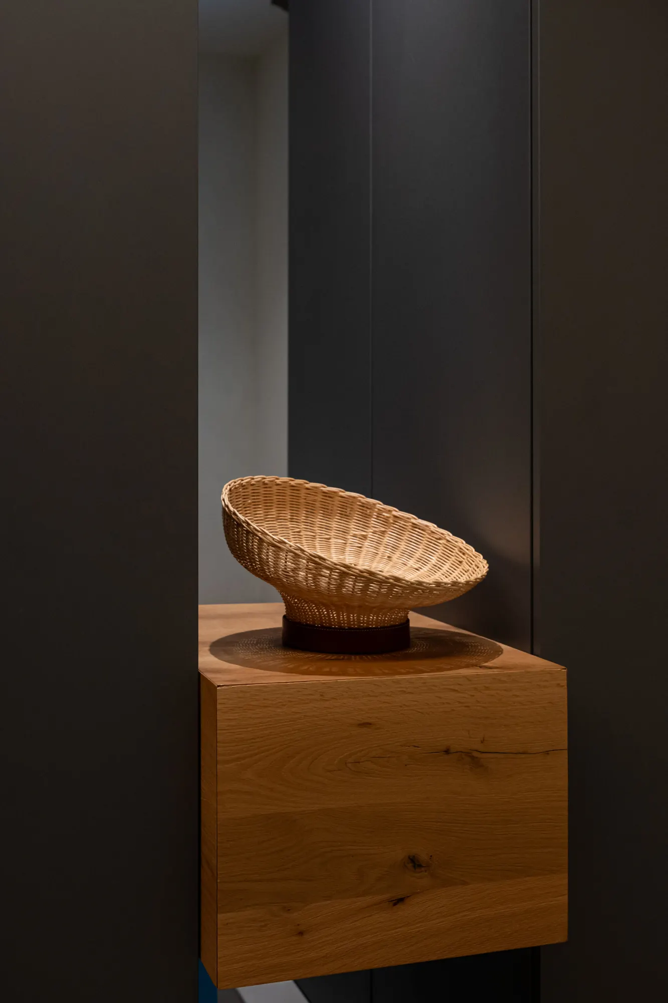 Wicker bowl on a solid oak block against a dark background