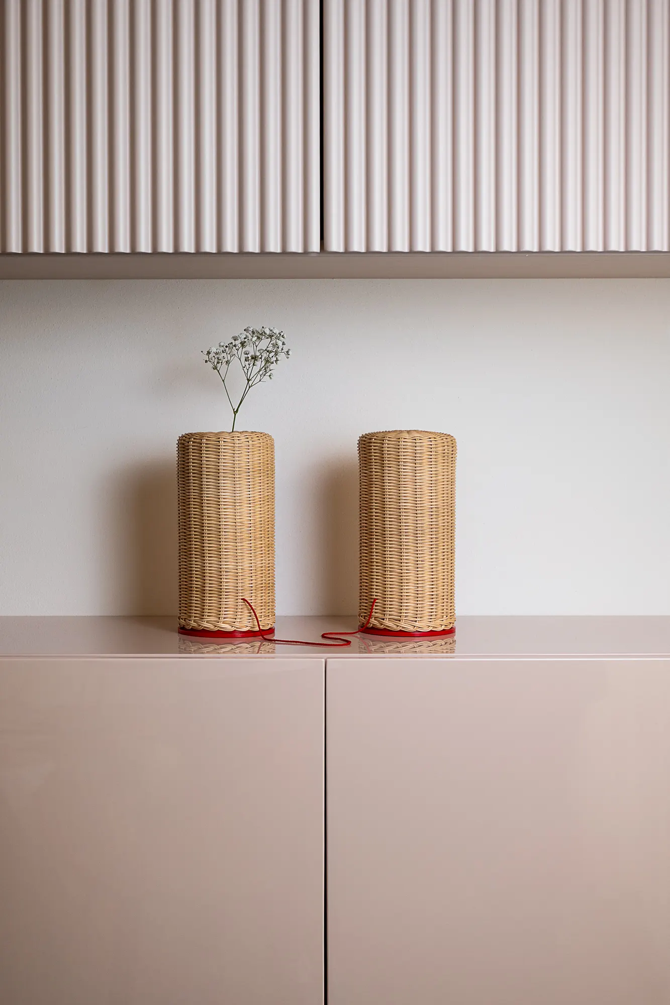 Two cylindrical rattan lamps on a pink sideboard below fluted cabinet doors