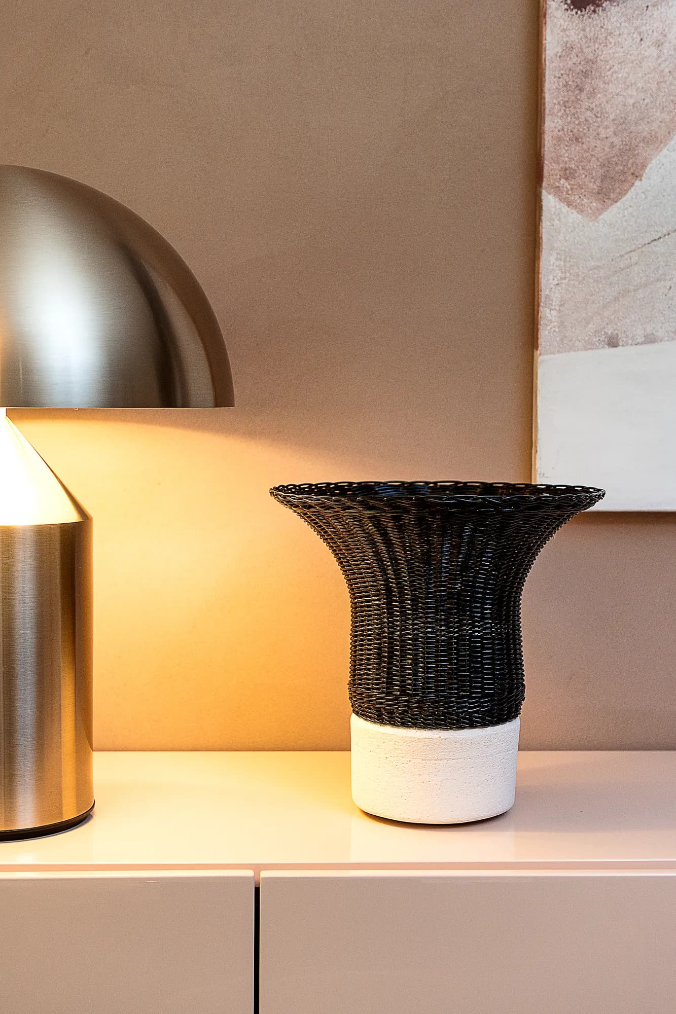 Black woven vase under a brass dome lamp