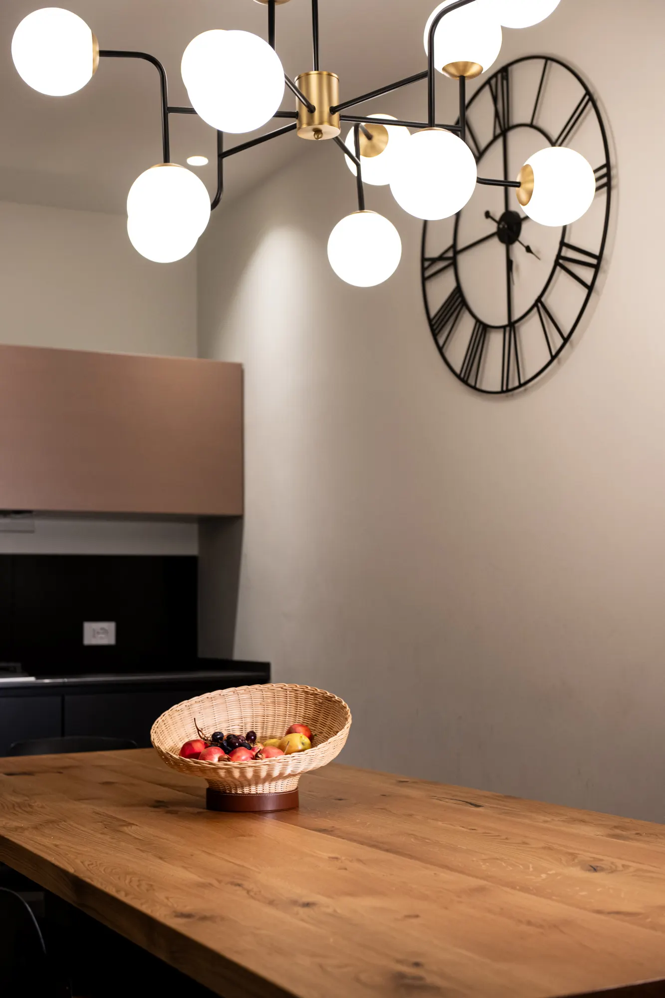 Fruttiera intrecciata su un tavolo di rovere, lampadario e orologio da parete sullo sfondo