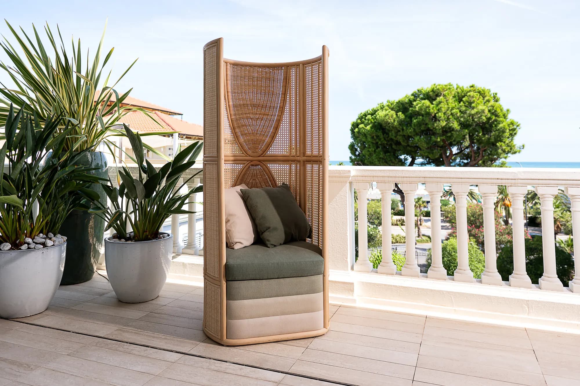 Poltrona paravento intrecciata su una terrazza sul mare, fra palme in vaso e una balaustra