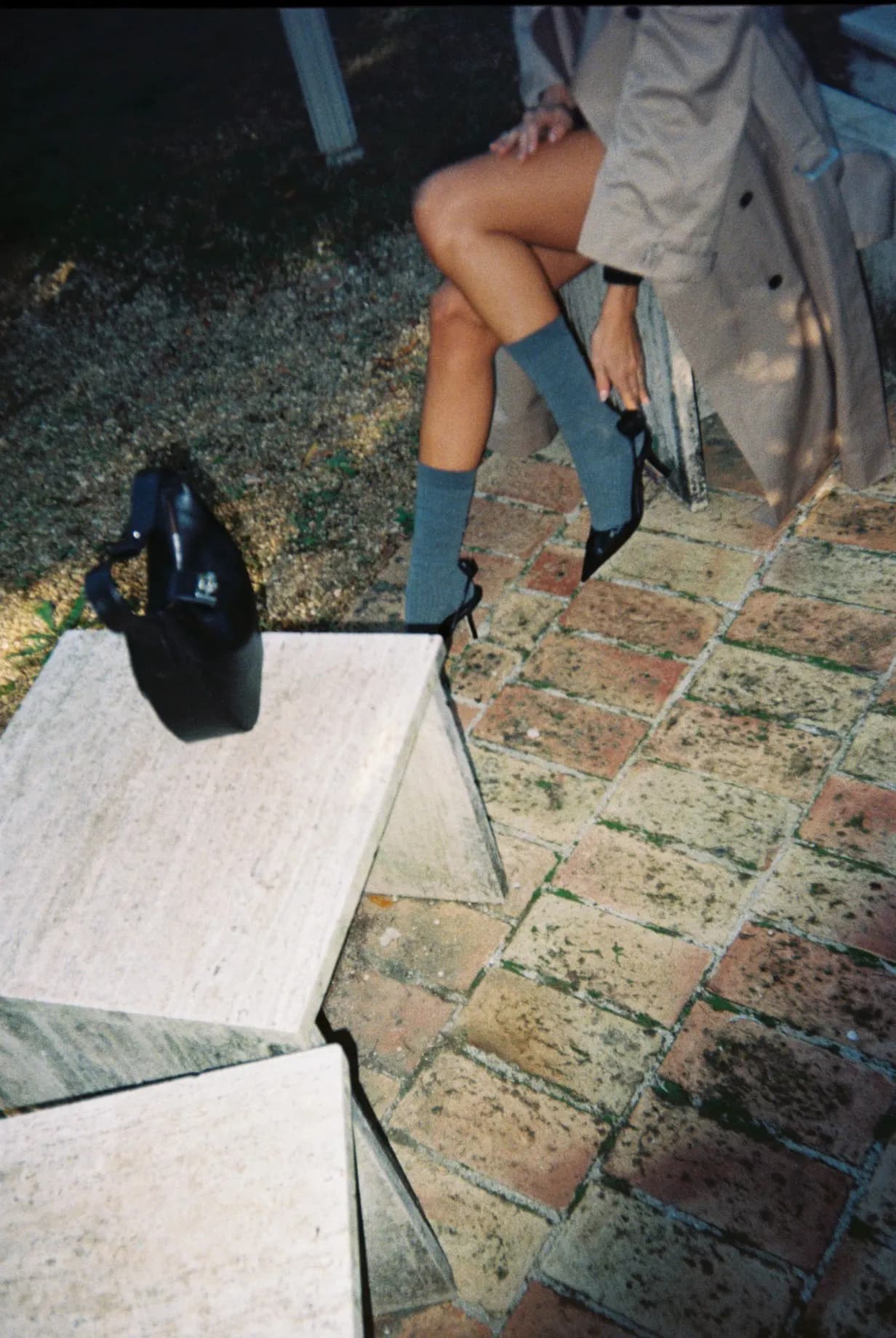 Shot on film: legs in socks and mules on a terracotta floor, black bag on the ground