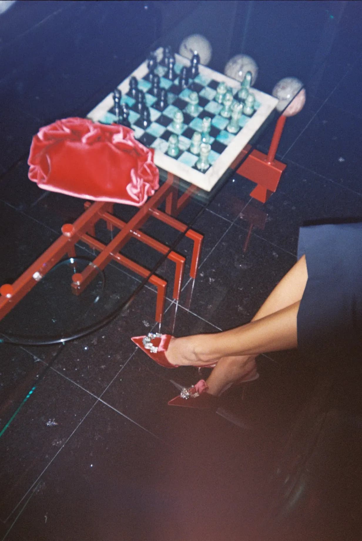 Flash shot on film: chessboard on a small table and red clutch, night interior