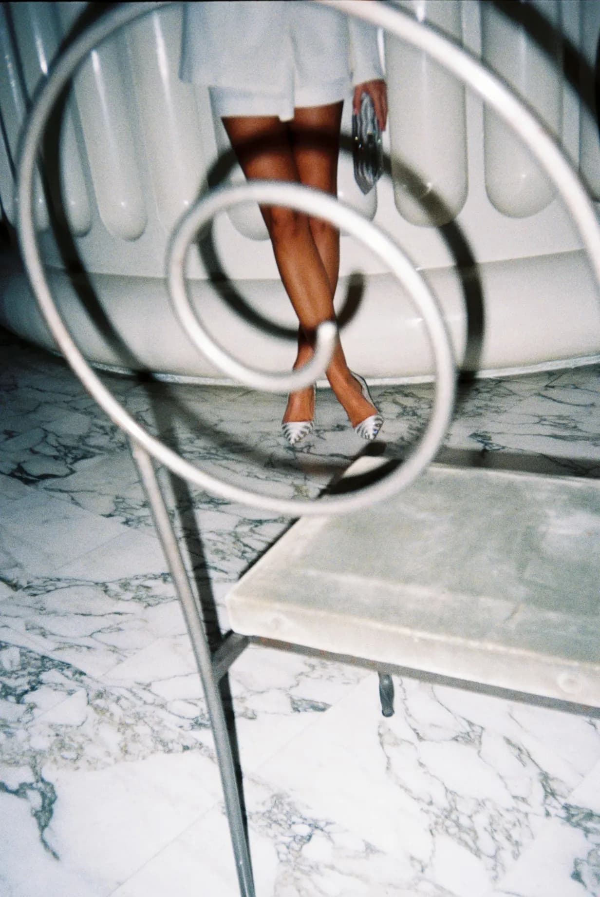 Shot on film: legs reflected in a curved structure on a marble floor