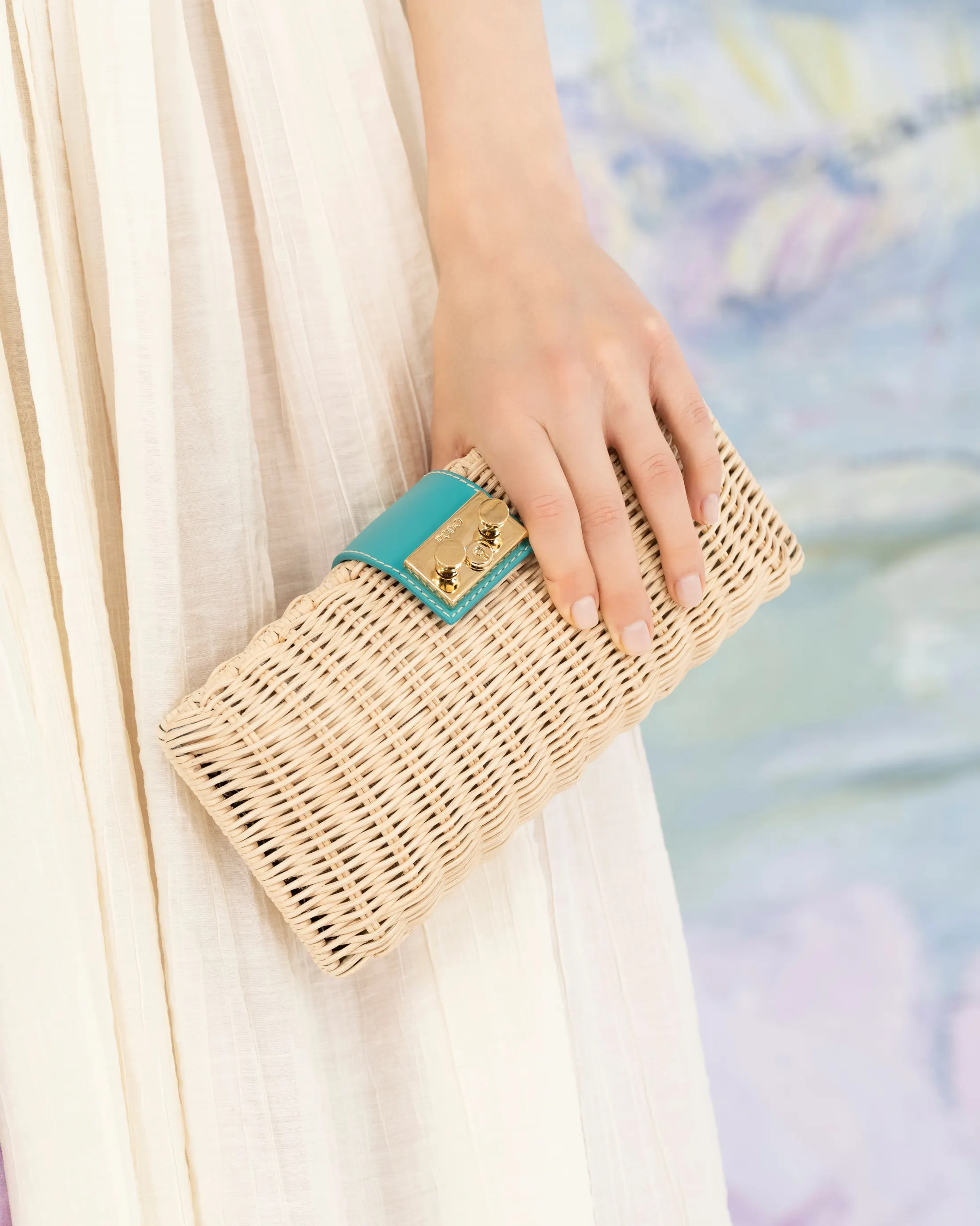 Woven straw clutch held in front of a backdrop reproducing Monet’s water lilies