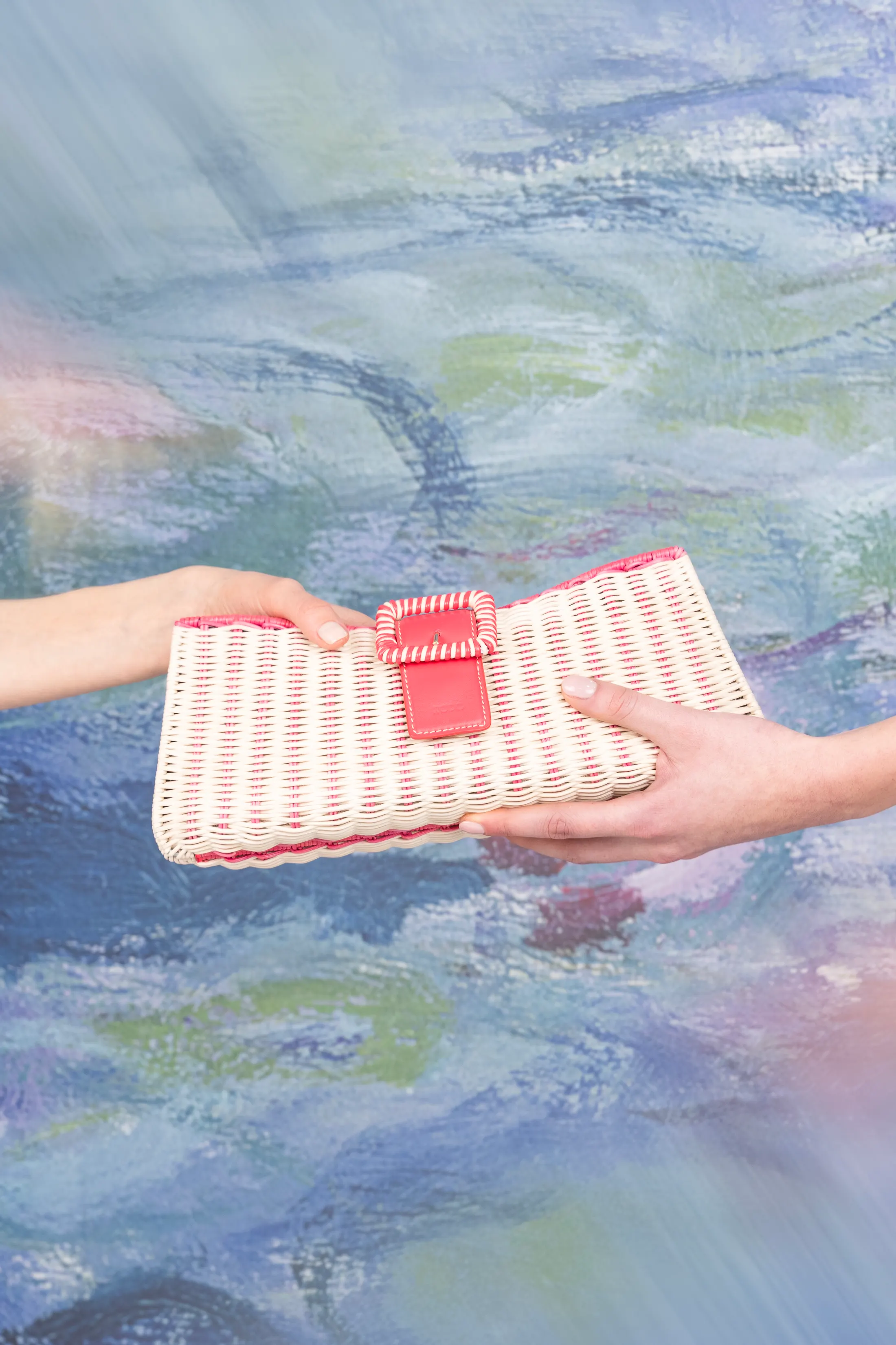 Two hands offering a white and red woven clutch in front of the water lilies