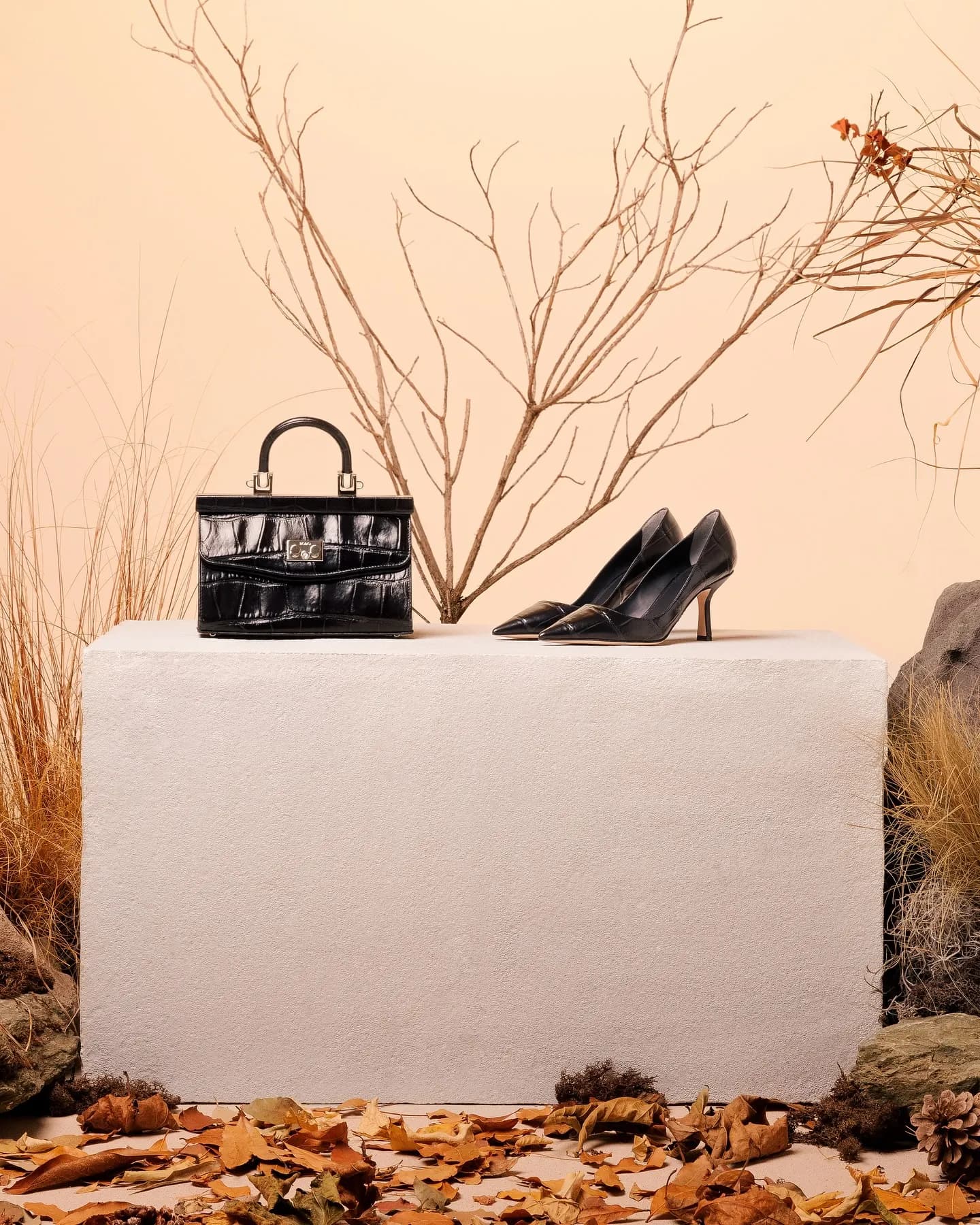 Legs seated on a pale block with a ruched red clutch, among dried grasses and stones