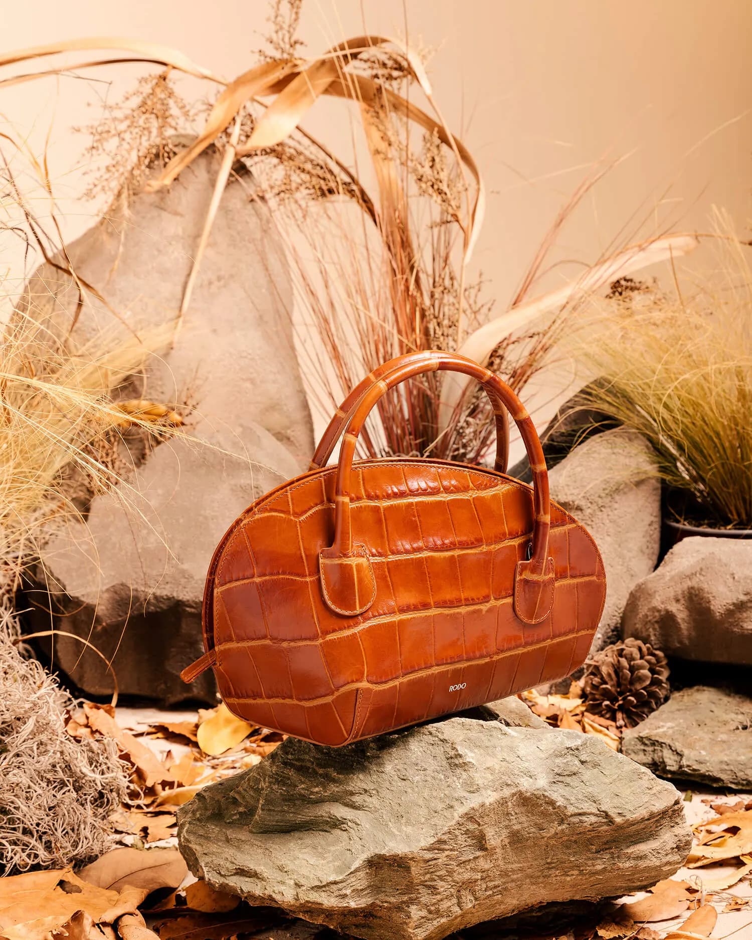 Tan leather bowling bag on a rock, among dried ears of wheat and leaves