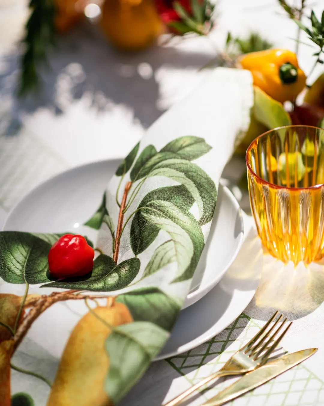 Detail of plate and amber glass on a leaf-print cloth, with fruit