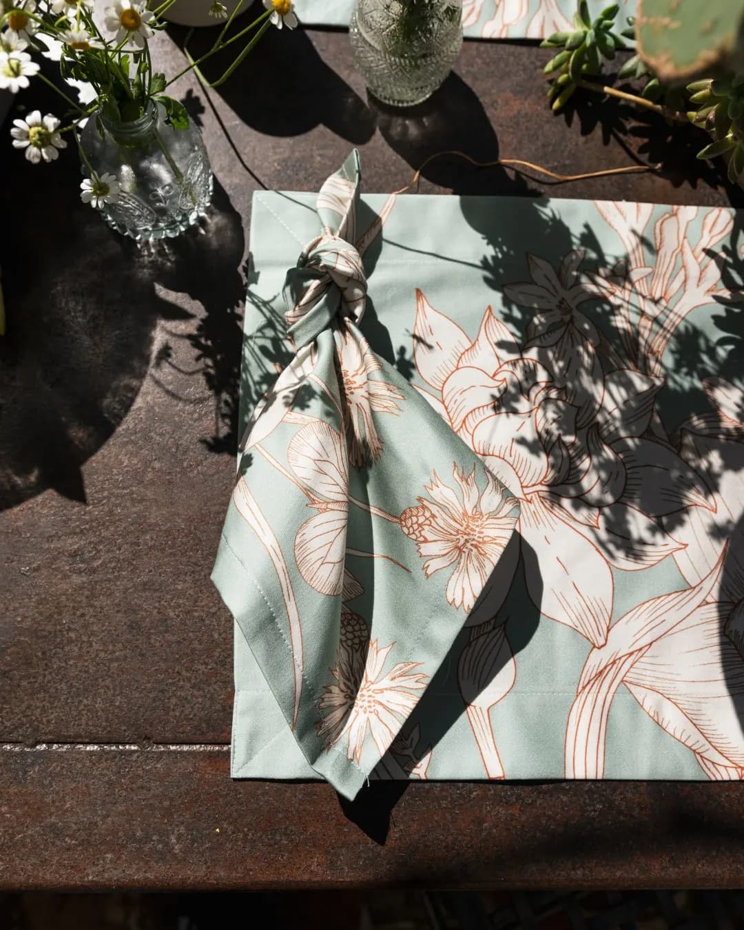 Sage green napkin tied in a knot, leaf shadows on the table